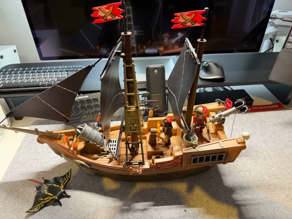 Gesamtansicht des aufgebauten Piratenschiffs mit schwarzen Segeln, roten Flaggen und einer Krakenfigur vor dem Bug.